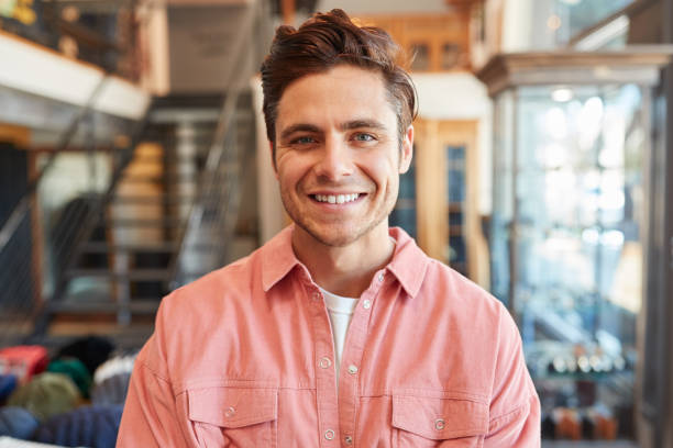 istockphoto-1230749818-612×612 Portrait Of Smiling Male Owner Of Fashion Store Standing In Front Of Clothing Display